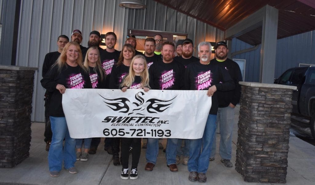 Swiftec staff wearing shirts that say Tough Enough to wear Pink and holding a Swiftec sign