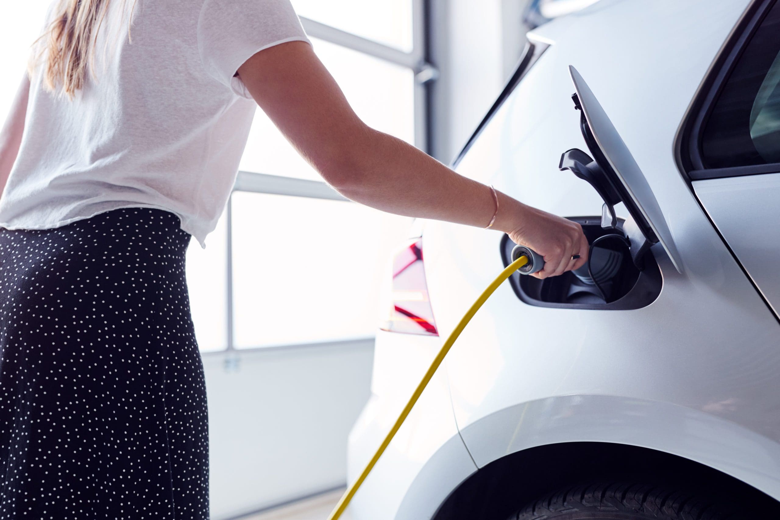 Closeup of woman charging electric vehicle with cable in garage at home