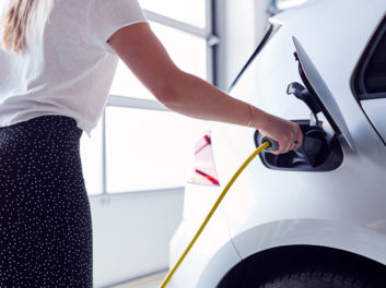 Close Up Of Woman Charging Electric Vehicle With Cable In Garage At Home